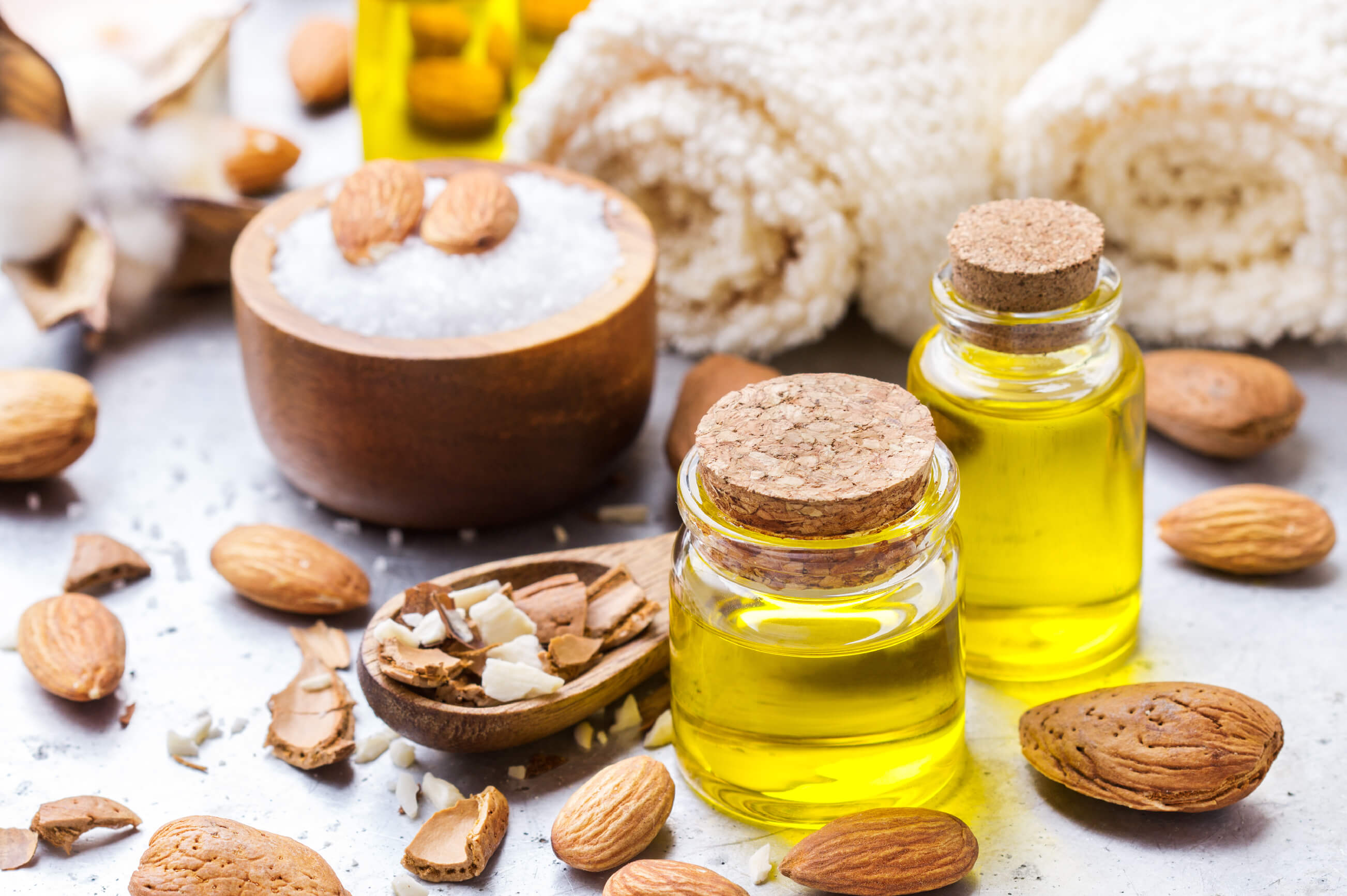 Two small jars of almond oil surrounded by loose almonds